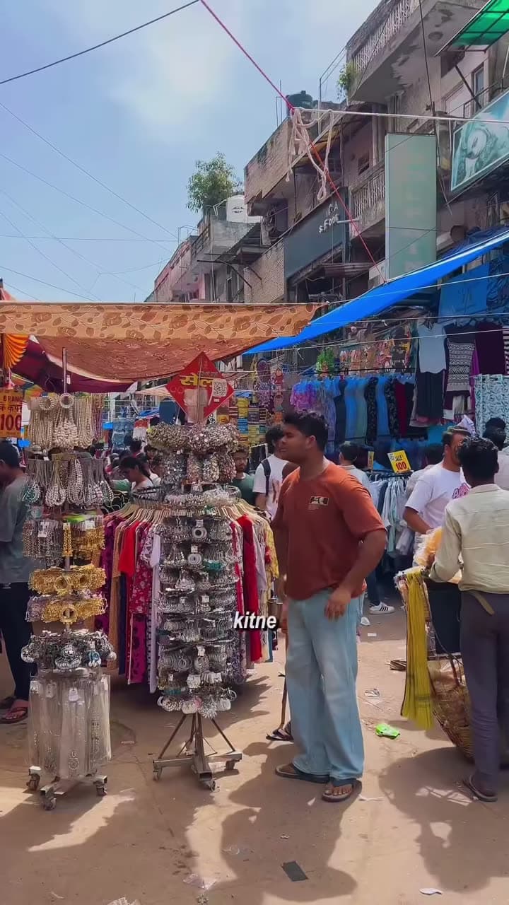 This is the creator's video. A man stands at a jhumka stall in a busy Sarojini Nagar lane, with a small subtitle near the bottom.